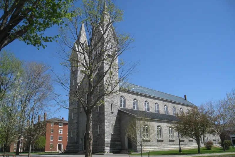 The granite Bowdoin College Chapel in Brunswick, Maine, with its twin spires among spring trees.