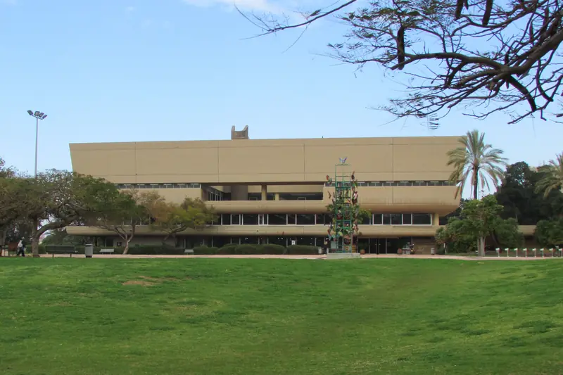 The Sourasky Central Library at Tel Aviv University, a long sand-colored building beyond a wide lawn and palm trees.